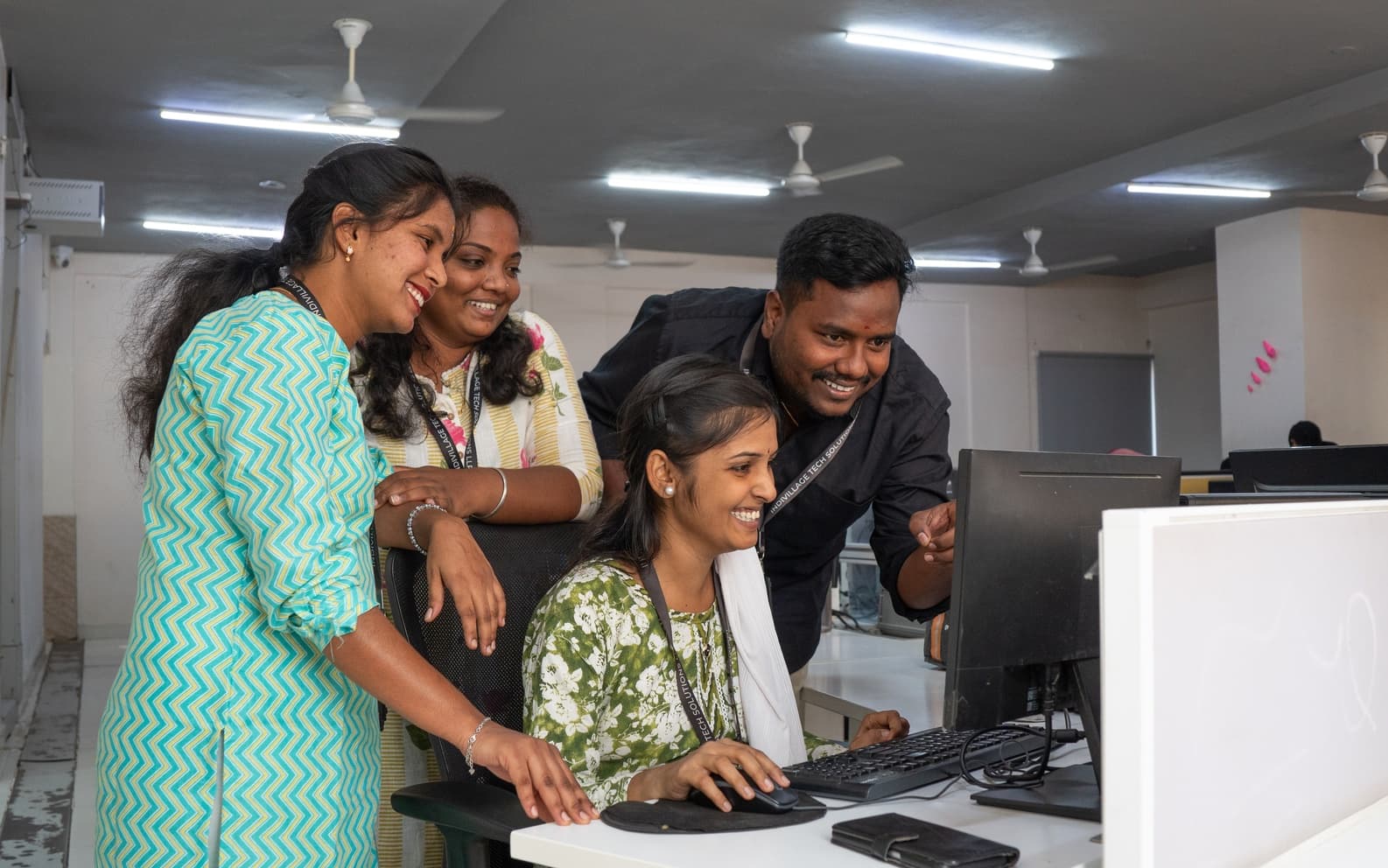 IndiVillage AgTech specialist woman demonstrating crop analysis to colleague, reviewing aerial imagery and field data on twin-monitor workstation
